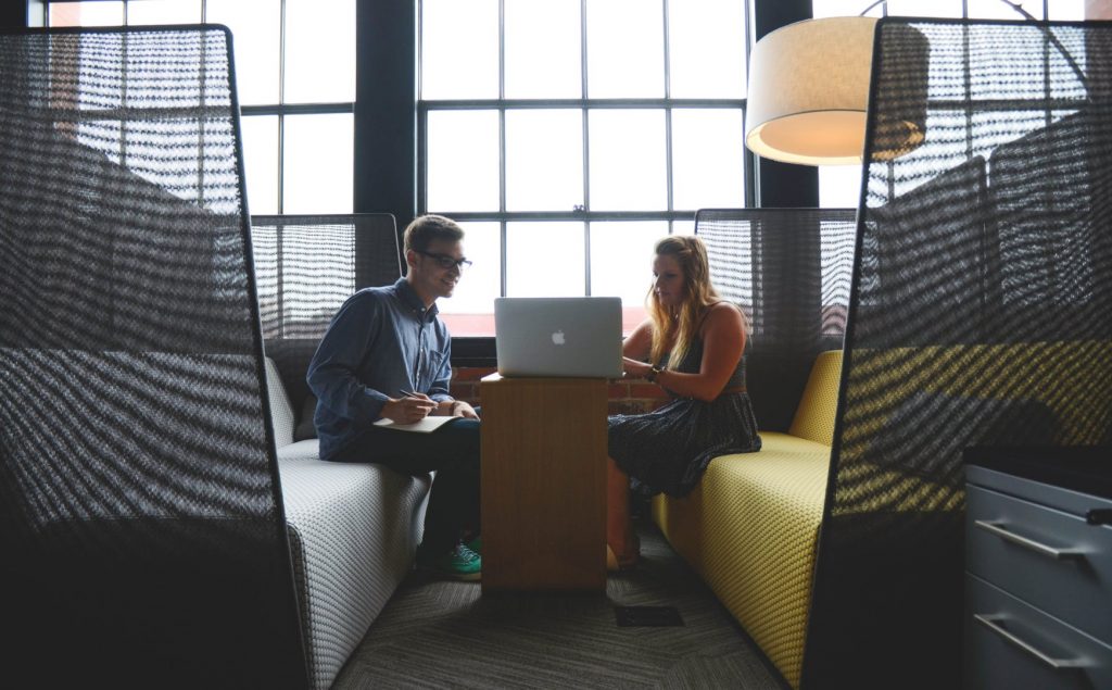 Two coworkers talking and writing on a laptop